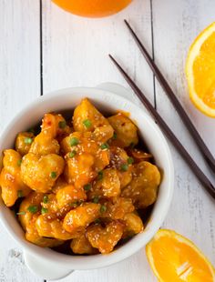 orange chicken in a white bowl with chopsticks next to it and an orange