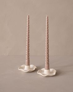 two pink candles sitting on top of each other in front of a beige wall and floor