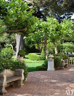 a park bench sitting on top of a brick walkway next to lush green trees and bushes