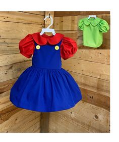 two children's dresses hanging on a wooden wall