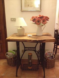 an old sewing machine table with flowers in a vase on top and magazines under it