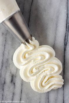 whipped cream being spread on top of a cupcake with a pastry mixer in the background