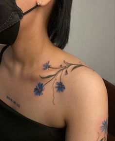 a woman with blue flowers on her chest and behind her ear is a black mask