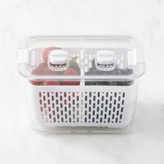 two plastic containers filled with fruits and vegetables on a white counter top next to each other