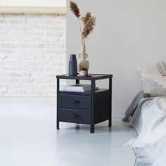 a black table with two drawers and a vase on it next to a white brick wall