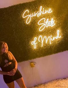 a woman standing in front of a fake grass wall with the words sunshine state of mind written on it