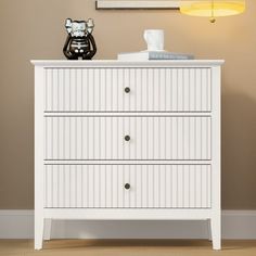 a white chest of drawers in a room with a painting on the wall behind it