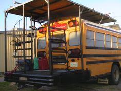 a yellow school bus parked in a parking lot with its doors open and luggage on the back