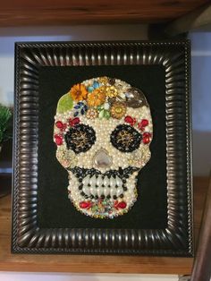 a beaded sugar skull is displayed in a frame on a shelf with other items