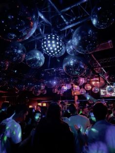 people are dancing at a party with disco balls hanging from the ceiling and lights on the ceiling