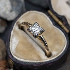 an engagement ring with a diamond in it sitting on a velvet case next to some rocks