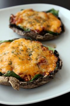 two stuffed mushrooms with cheese and spinach on them sitting on a white plate, ready to be eaten