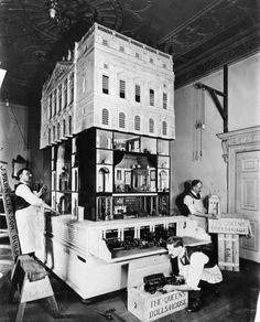 two women are working on a model of a house in an old fashioned room with other people around it