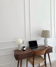 a laptop computer sitting on top of a wooden desk next to a vase with flowers