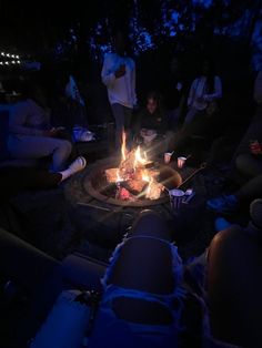 a group of people sitting around a fire pit in the dark with candles on it