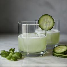 two glasses filled with cucumber juice and one has a slice of cucumber on the rim