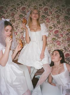 two women in white dresses are eating donuts while another woman sits on the floor