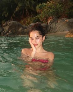 a woman is in the water with her hand on her face and looking at the camera