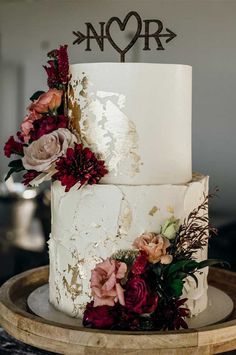 a white wedding cake with flowers and an arrow topper on a wooden platter