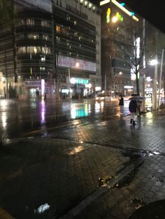 two people walking down the street in the rain at night with an umbrella over their head