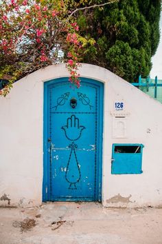 a blue door with a hand drawn on it in front of a white wall and tree