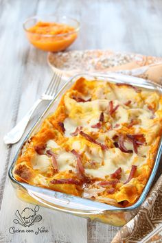 a casserole dish with bacon and cheese in it on a table next to silverware