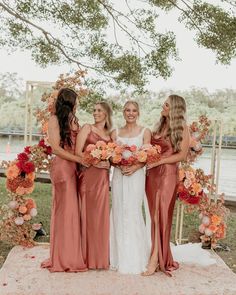 four bridesmaids standing in front of an arch with orange flowers and greenery