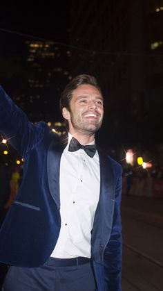 a man in a tuxedo waves to the crowd as he stands outside at night