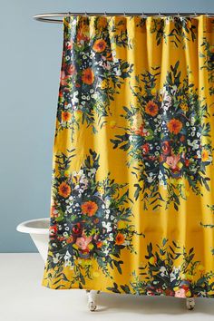 a yellow shower curtain with flowers on it in front of a white bathtub and blue wall