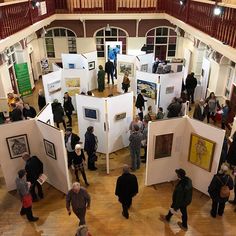 a group of people standing around looking at art on display in an open area with wooden floors