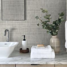 a bathroom with marble counter tops and white towels on the shelf next to it is a vase filled with green leaves