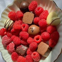 a bowl filled with assorted chocolates and raspberries