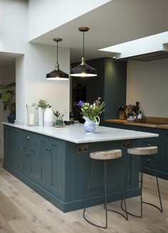 a large kitchen with blue cabinets and white counter tops, two stools in front of the island