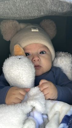 a baby in a car seat holding a stuffed animal and wearing a knitted hat