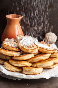 a plate full of pancakes with powdered sugar on top and a vase in the background