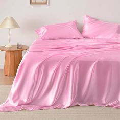 a bed with pink sheets and pillows in a room next to a lamp on a table