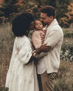 a man and woman are holding a baby in their arms while standing in the grass