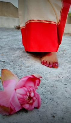 a pink flower laying on the ground next to a person's feet