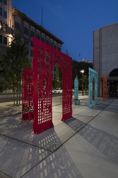 three red metal sculptures in the middle of a plaza at night with buildings in the background