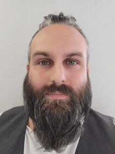 a man with grey hair and beard wearing a gray jacket is looking at the camera