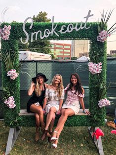 three women are sitting on a bench in front of a sign that says smokeout