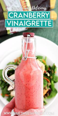 a hand holding a bottle filled with cranberry vinaigrette next to a salad