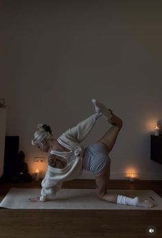 a woman is doing yoga on a mat with candles in the room behind her as well