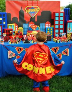 a young boy dressed up as a superman standing in front of a table with decorations