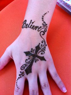 a woman's hand with a tattoo on it that says believe and has a cross