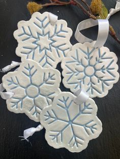 three snowflake ornaments are hanging on a tree branch with white ribbon around them