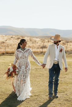 a bride and groom holding hands while walking through the field