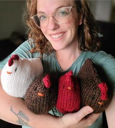 a woman wearing glasses holding three knitted chickens