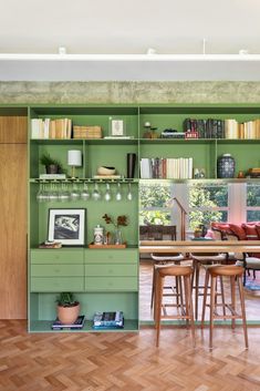 an open kitchen with green cabinets and wooden flooring in the center is a dining table, bar stools, bookshelves, and pictures on shelves