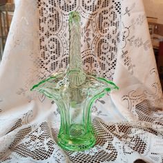 a green glass vase sitting on top of a lace covered table cloth next to a window